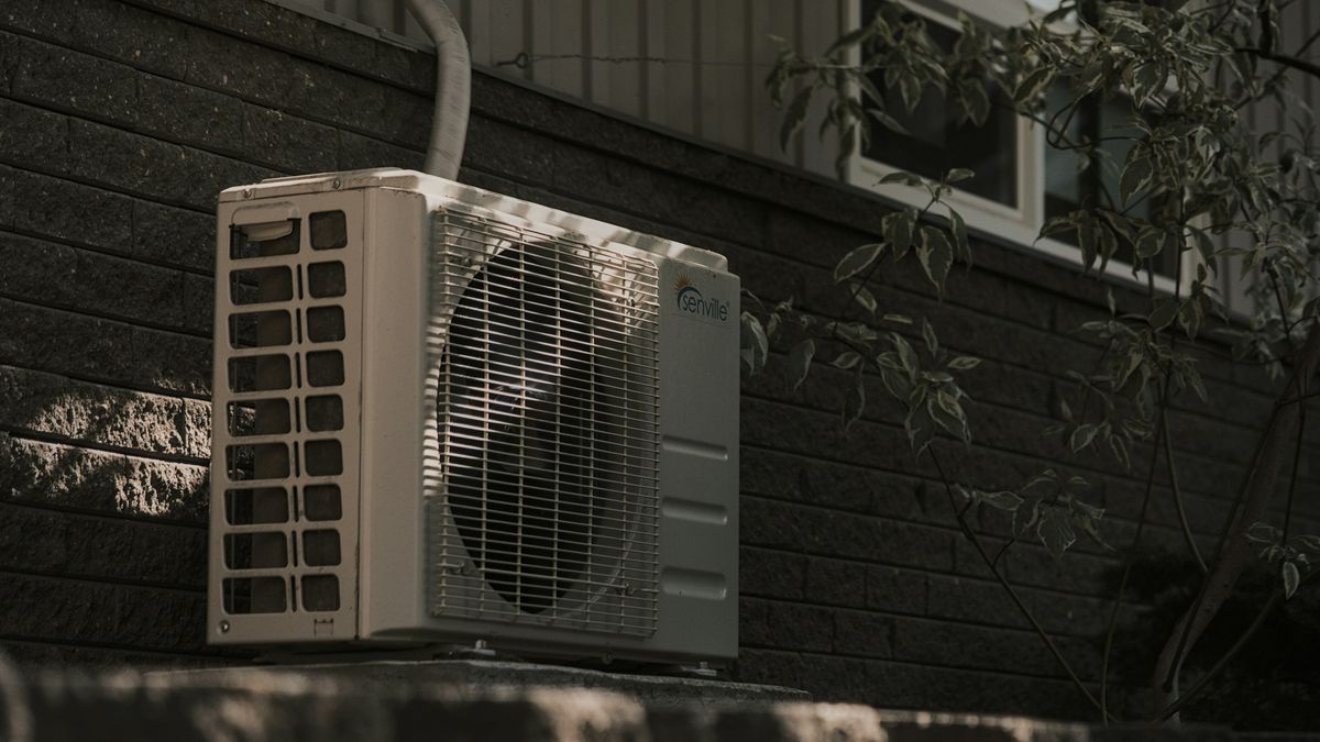 Ductless mini split outdoor condenser unit mounted against the dark siding of a house