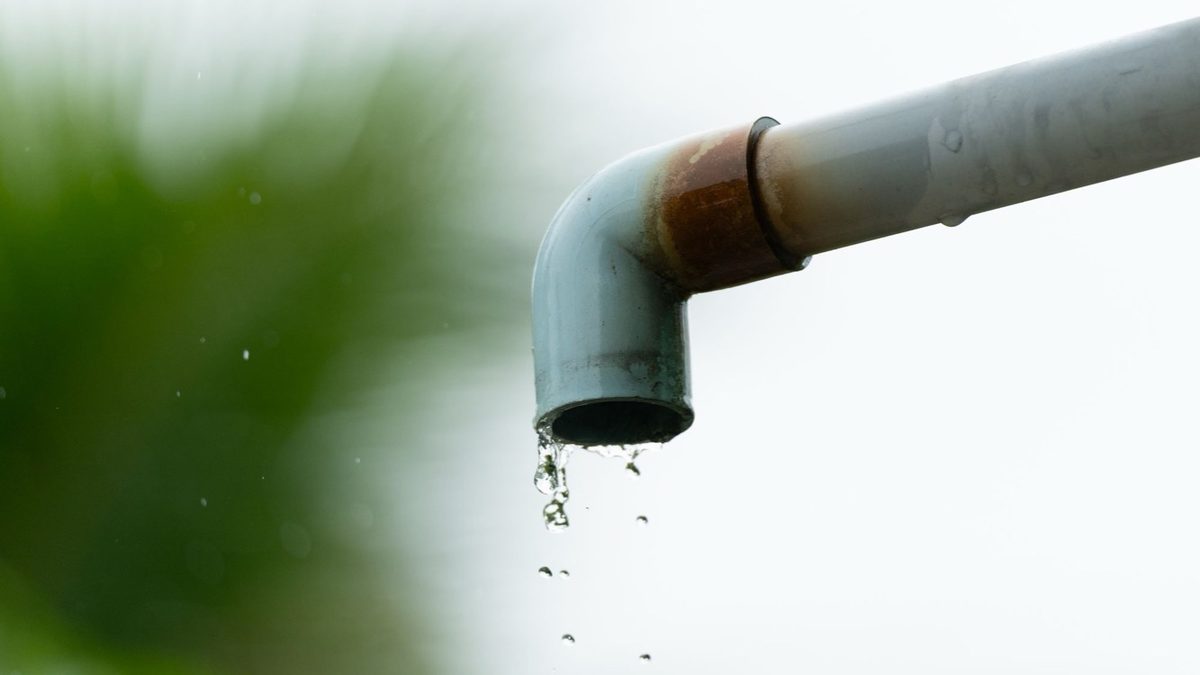 Gray PVC elbow pipe with water droplets dripping, part of a mini split drain line installation guide setup