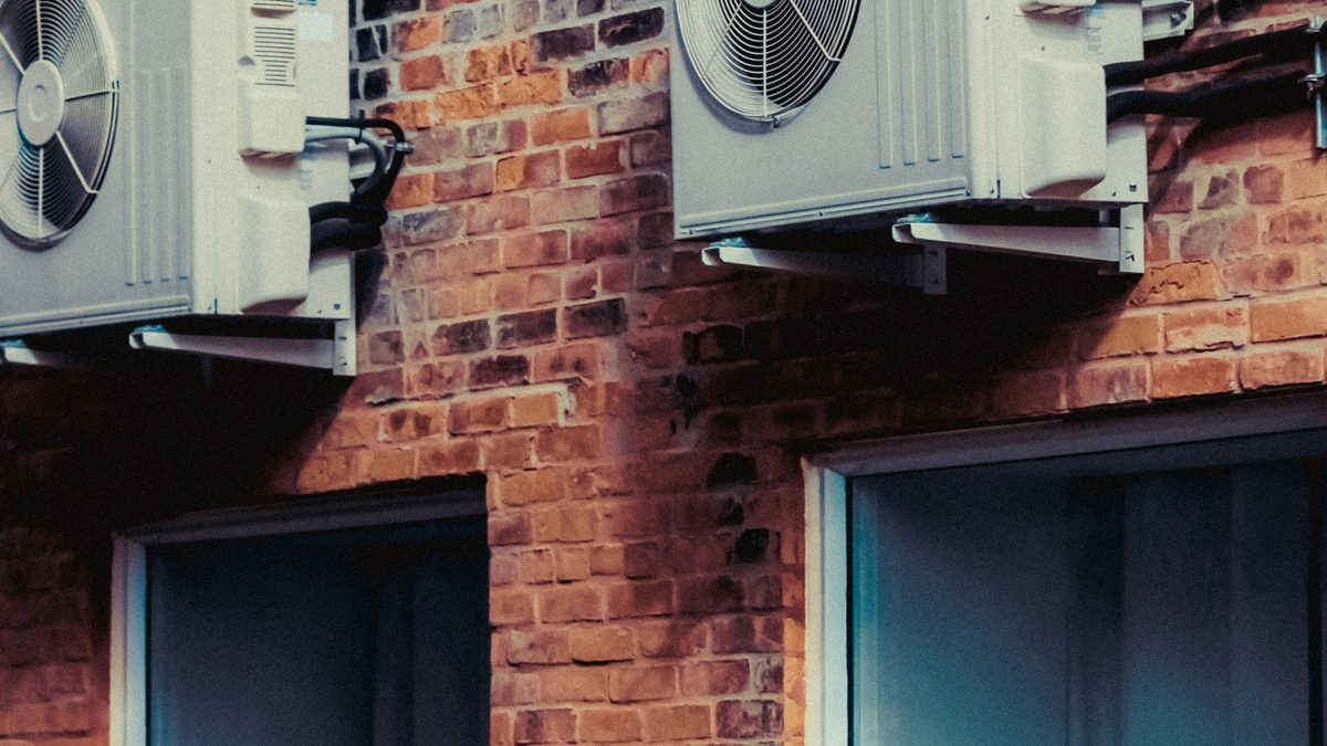 Two gray ductless mini split installation checklist condenser units mounted on a red brick wall above windows
