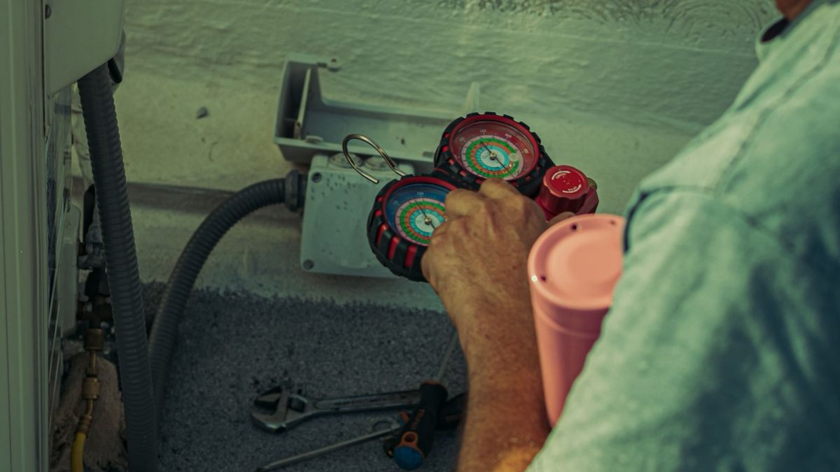 HVAC technician with manifold gauges connected to outdoor unit, using mini split installation tools on the ground nearby