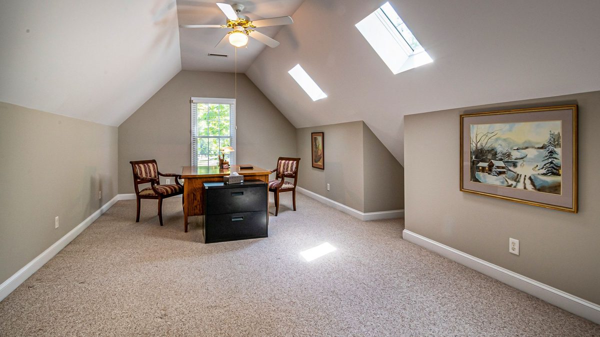 Finished bonus room with sloped ceilings, skylights, and ceiling fan with light, illustrating cooling a bonus room guide