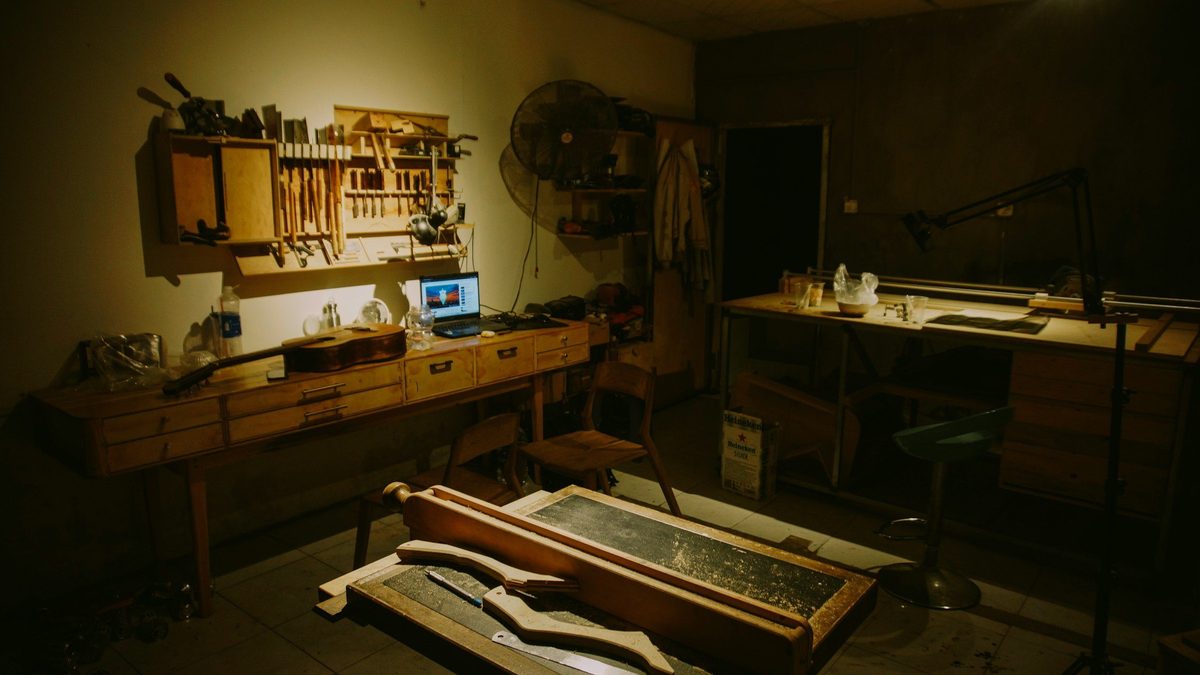 Industrial fan and laptop on wooden workbenches in a dim workshop, one way to cool a workshop without ductwork